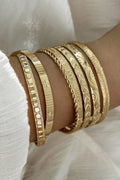 Gold bracelets on a wrist with a white fabric background