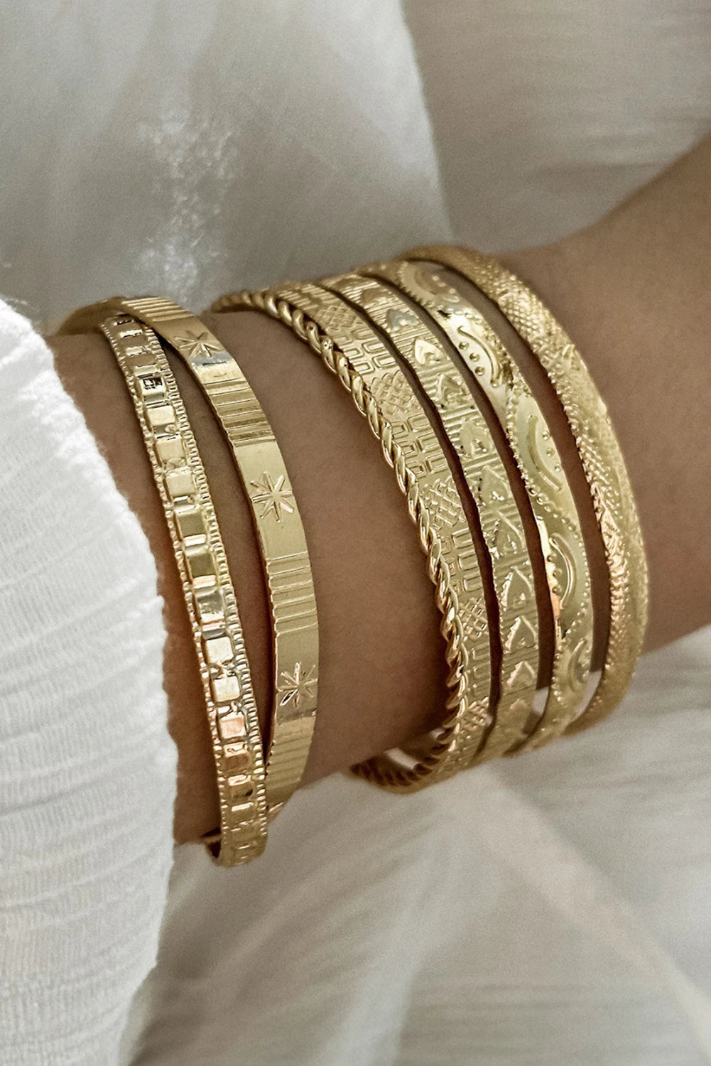 Gold bracelets on a wrist with a white fabric background