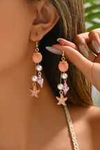 Close-up of a person wearing pink earrings with starfish and pearl details.