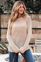 Woman wearing a beige knitted sweater and blue jeans outdoors.