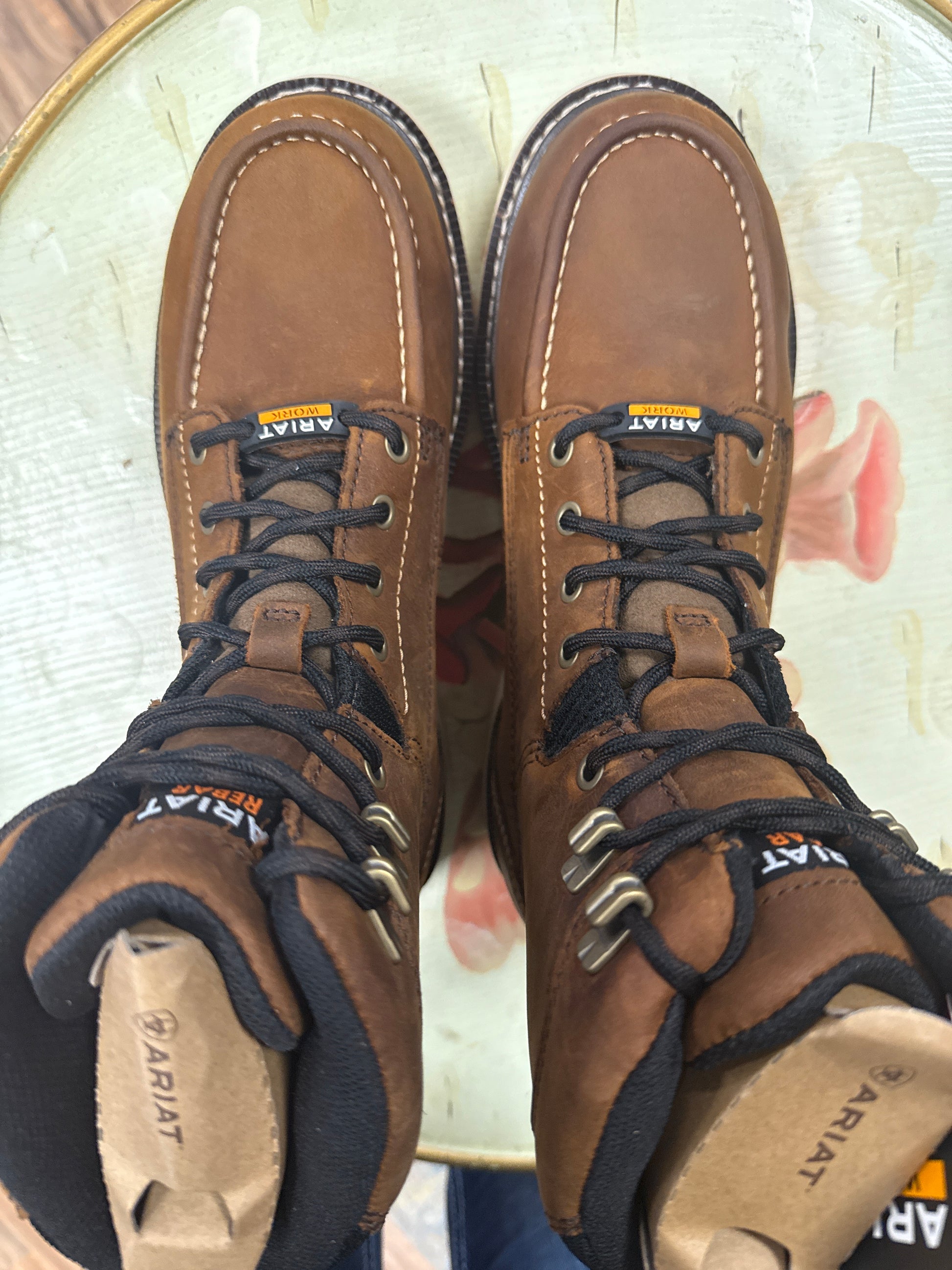 Pair of brown Ariat boots with laces on a light background