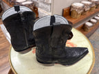 Black cowboy boots on a round white surface with a blurred background