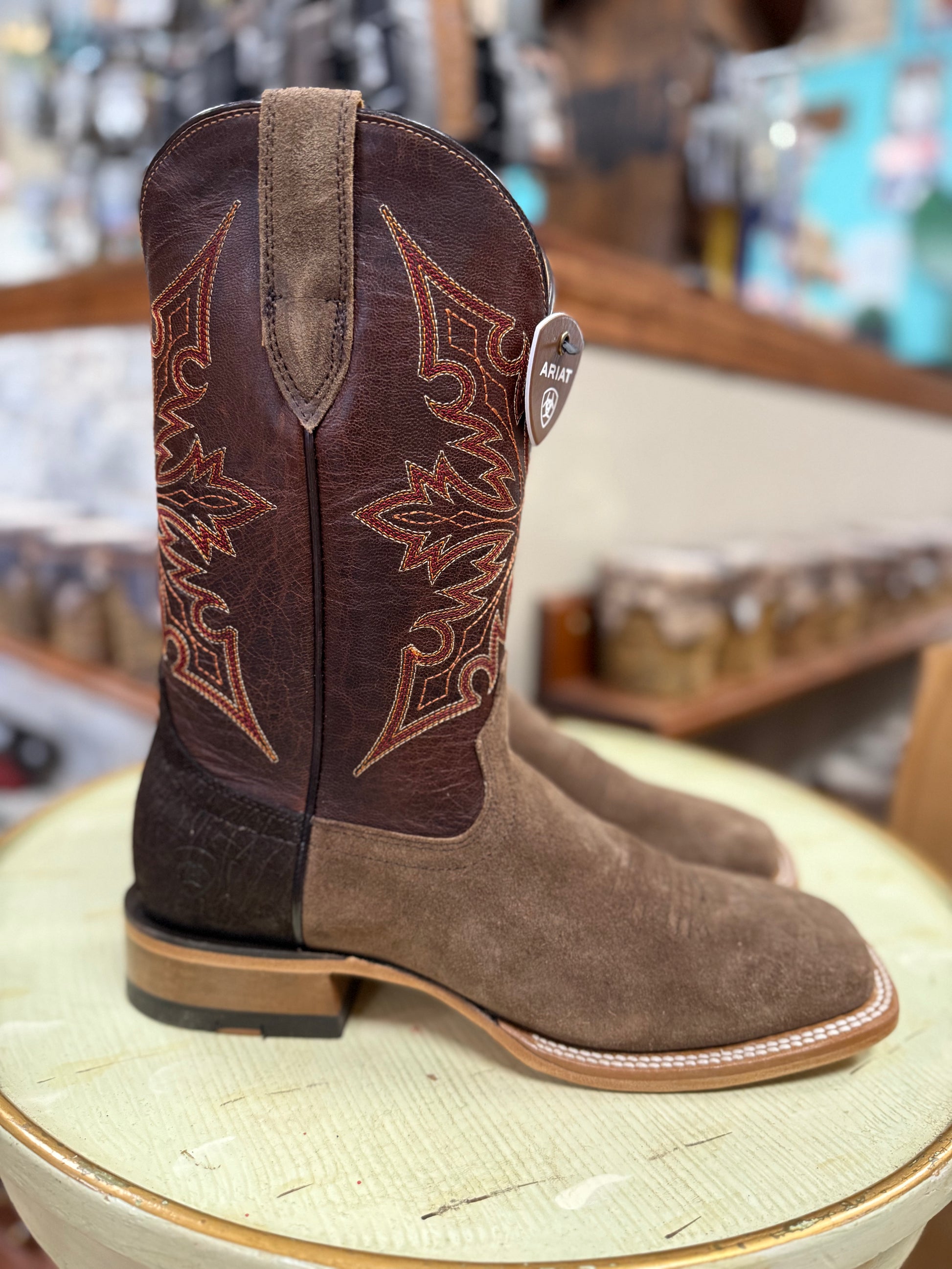 Brown cowboy boot with intricate stitching on a round surface in a store setting.