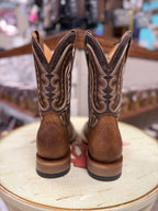 Pair of brown cowboy boots with intricate designs on a round surface.