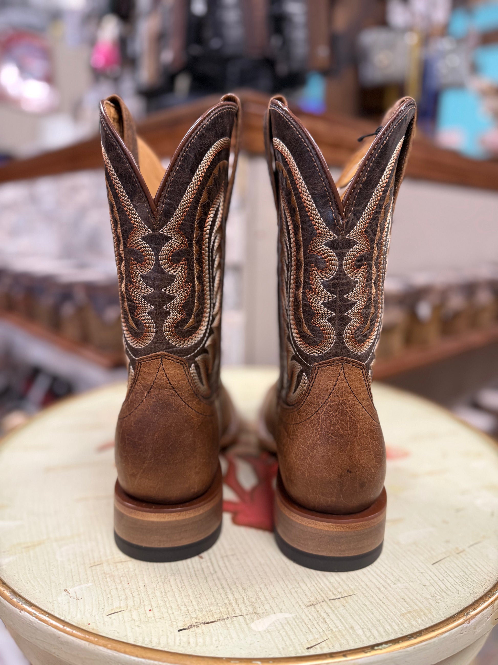 Pair of brown cowboy boots with intricate designs on a round surface.