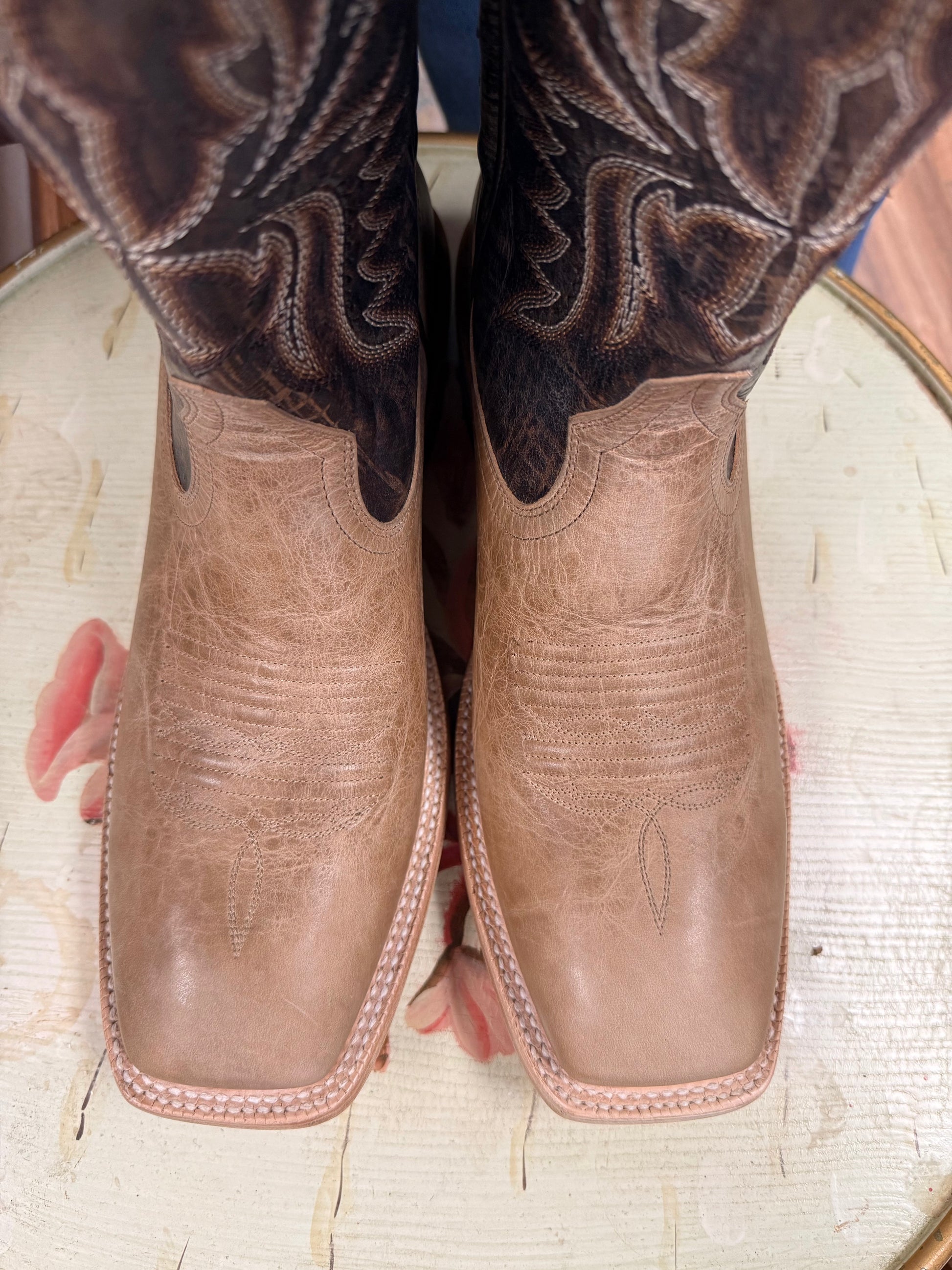 Close-up of brown leather cowboy boots with intricate stitching on a textured surface.