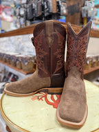 Pair of brown cowboy boots with intricate designs on a stool in a store setting.