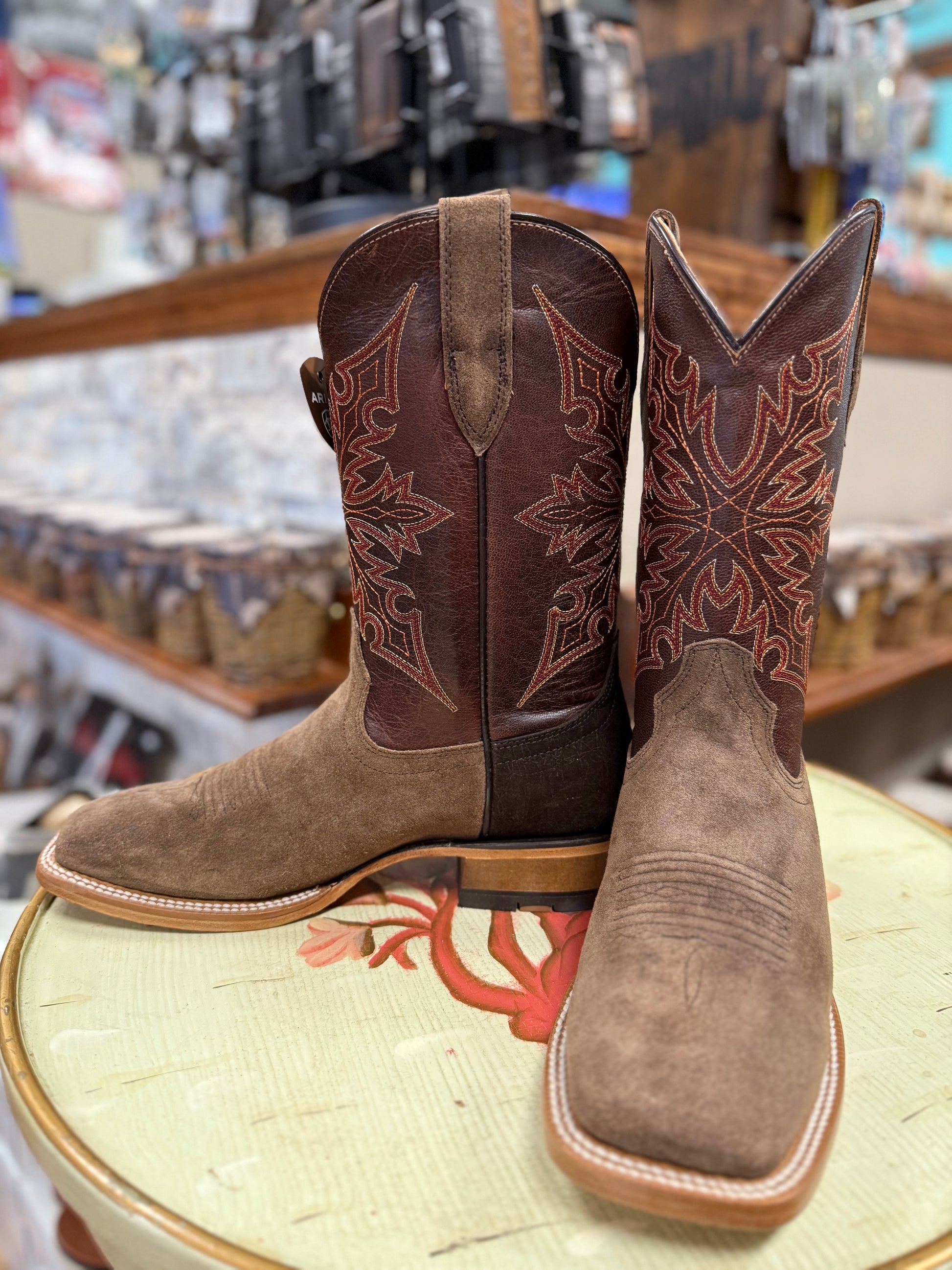 Pair of brown cowboy boots with intricate designs on a stool in a store setting.