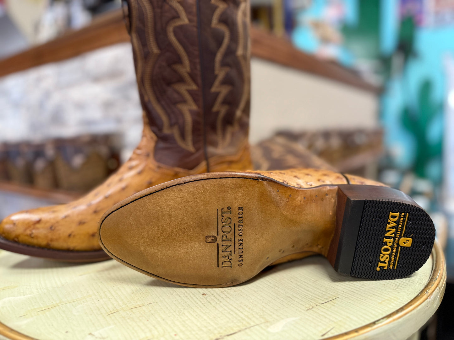 Brown cowboy boot with visible Dan Post logo on a wooden stool.