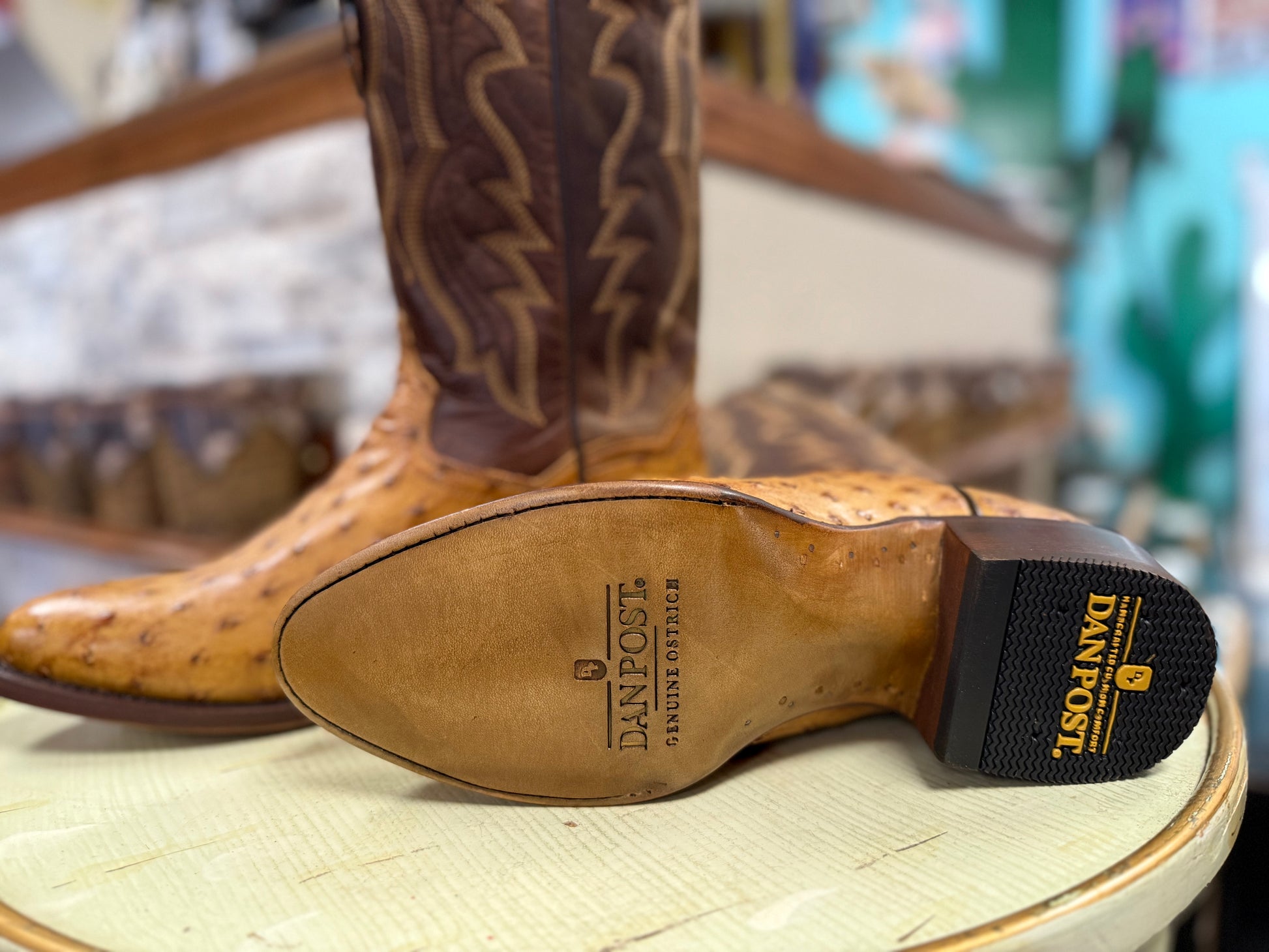 Brown cowboy boot with visible Dan Post logo on a wooden stool.