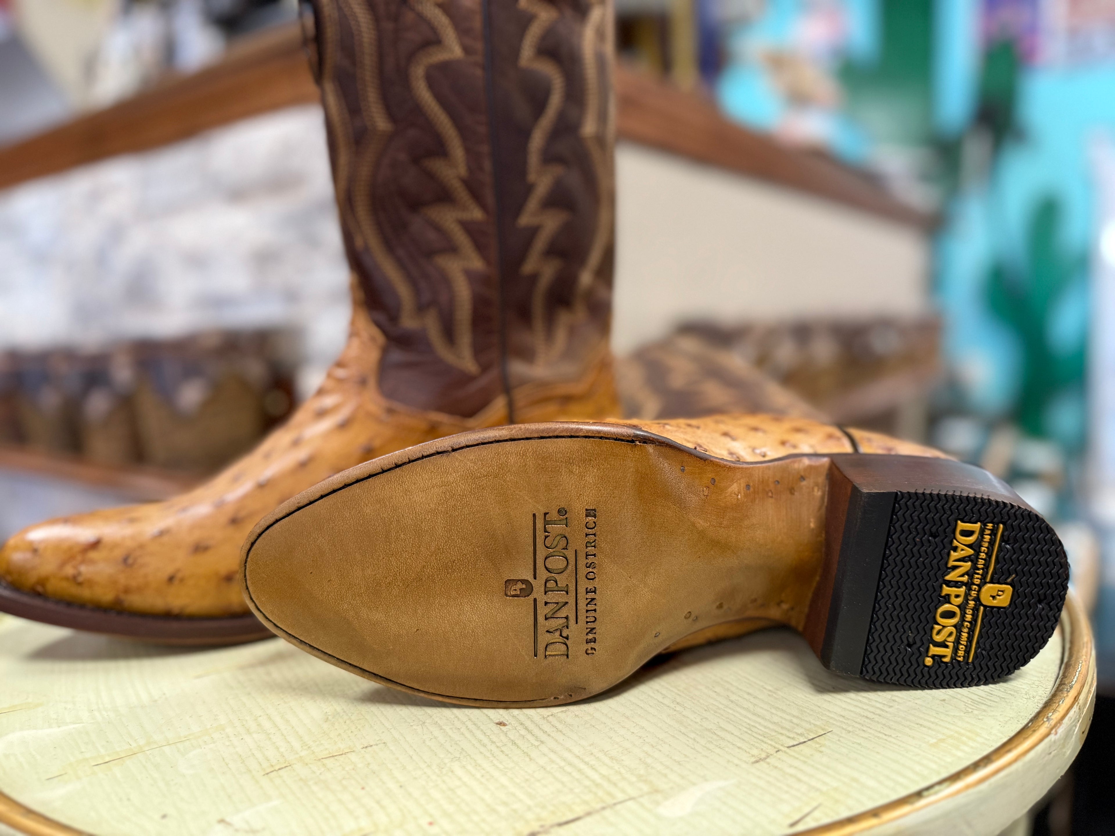 Brown cowboy boot with visible Dan Post logo on a wooden stool.