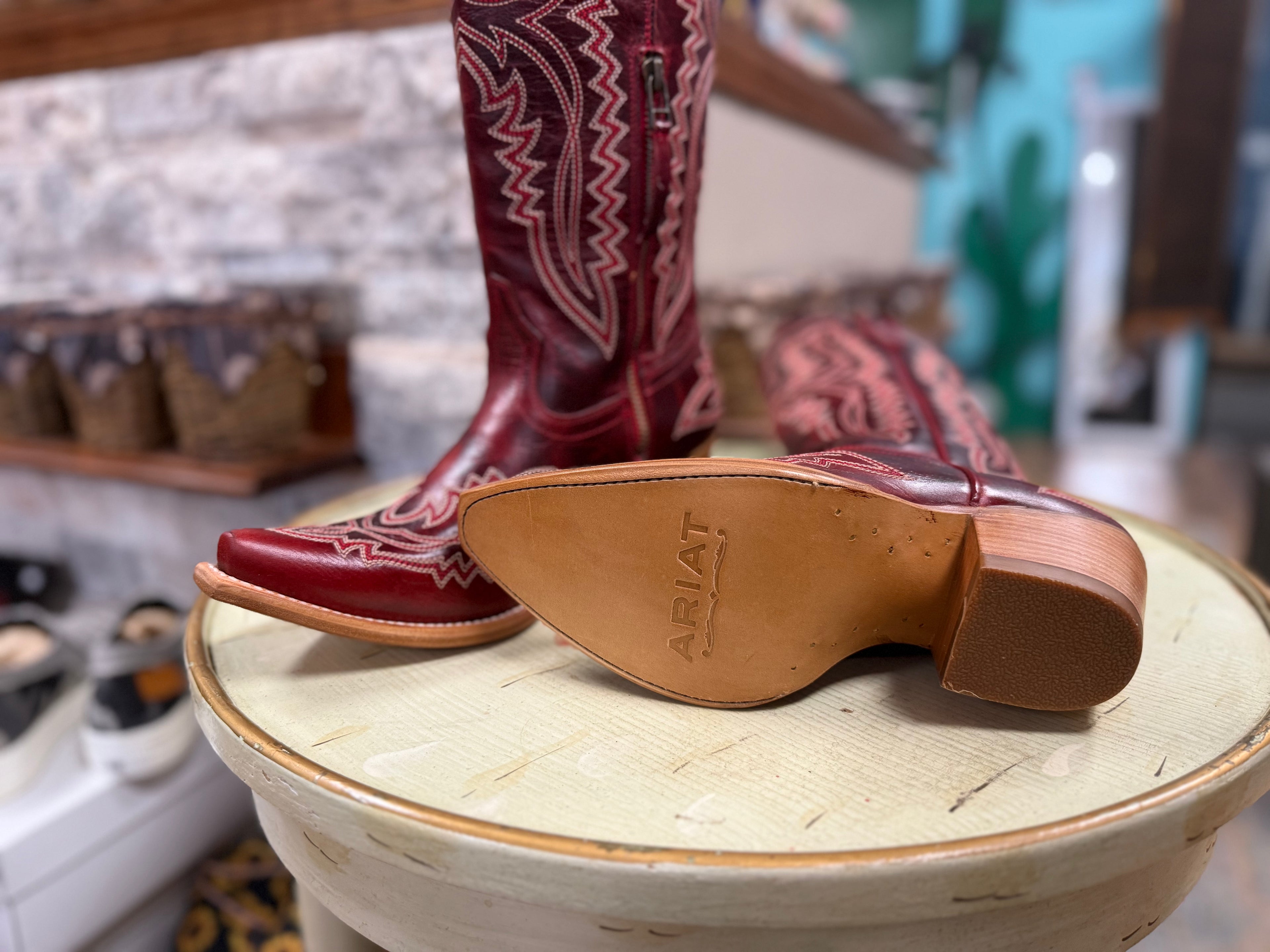Red cowboy boot with a visible 'Ariat' logo on a wooden stool.