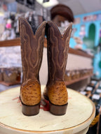 Pair of brown cowboy boots with embossed design on a round surface in a store setting.