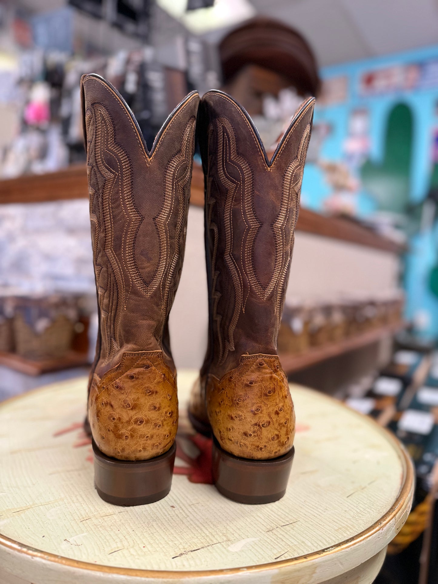 Pair of brown cowboy boots with embossed design on a round surface in a store setting.