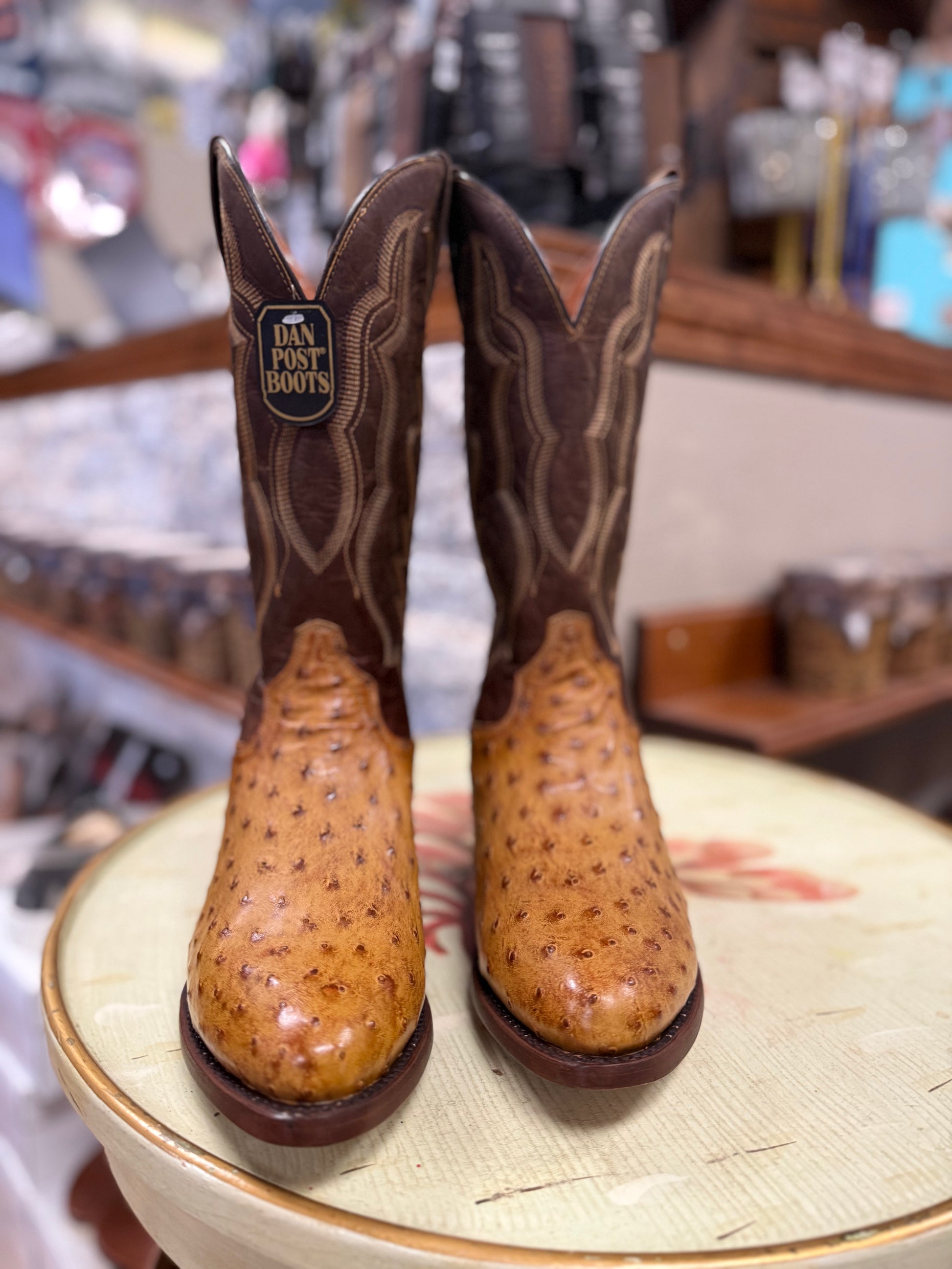 Pair of brown cowboy boots with a visible brand label on a round surface.