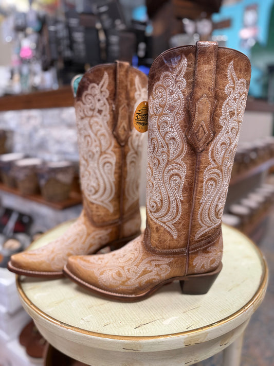 Pair of brown cowboy boots with white embroidery on a round wooden stool.