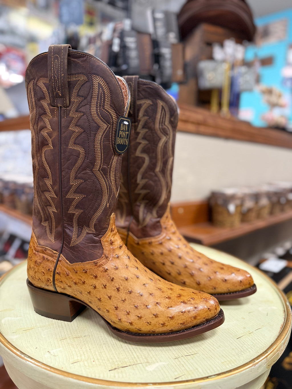 Brown and tan cowboy boot on a round white surface with a blurred store background