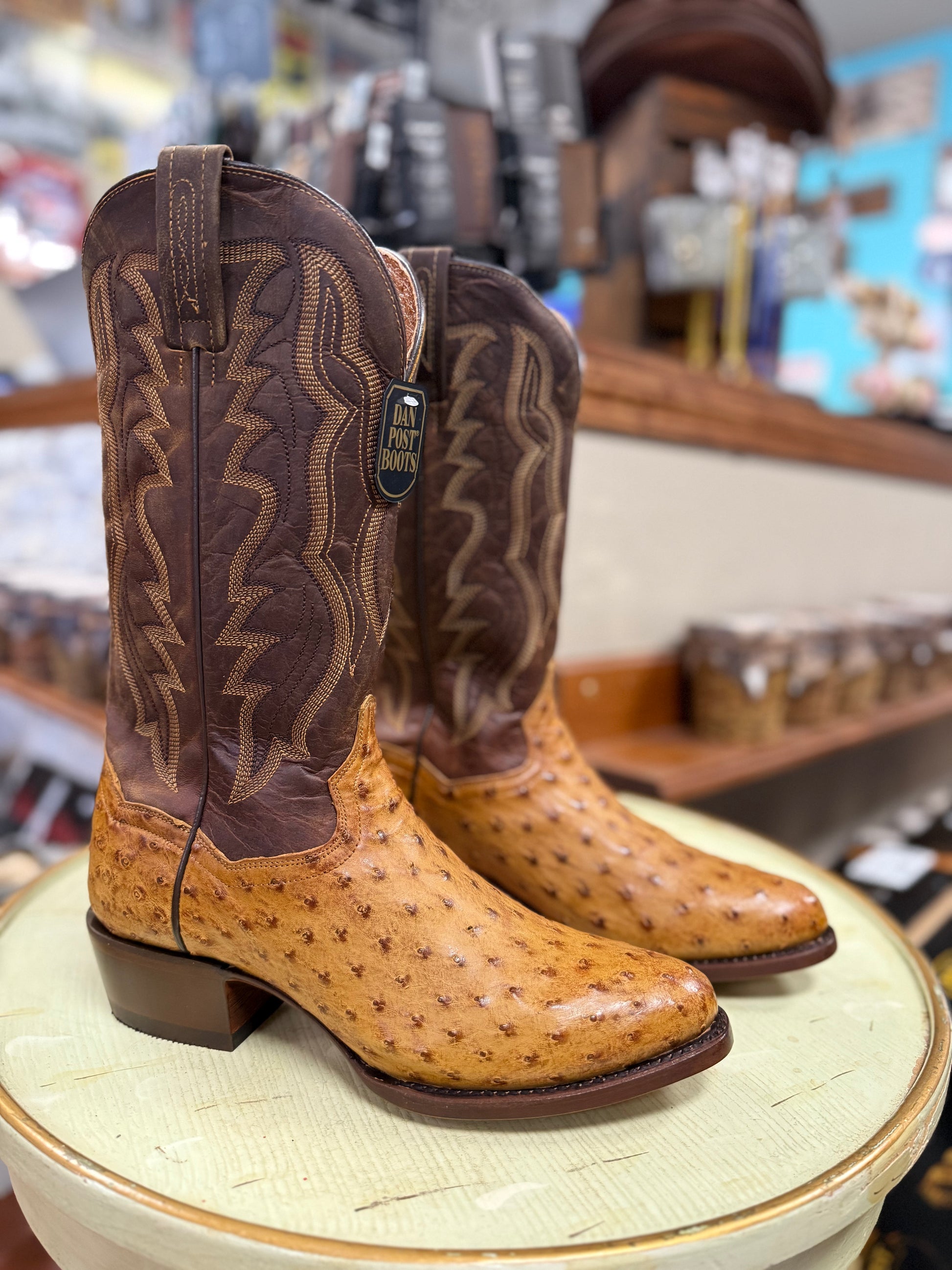 Brown and tan cowboy boot on a round white surface with a blurred store background