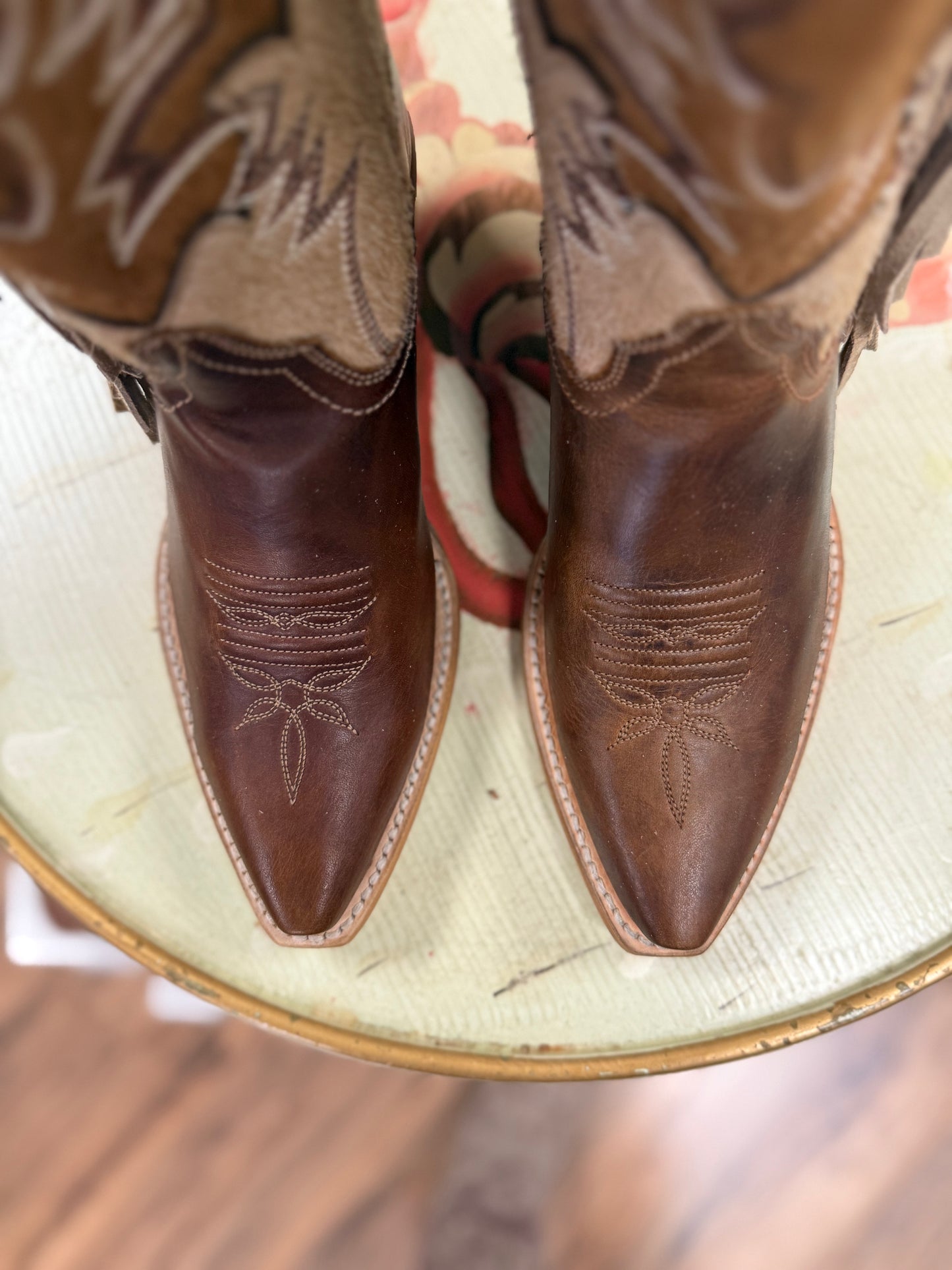 Brown cowboy boots with intricate detailing on a glass surface.