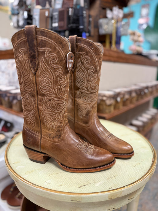 Brown cowboy boots with intricate designs on a round stool in a store setting.