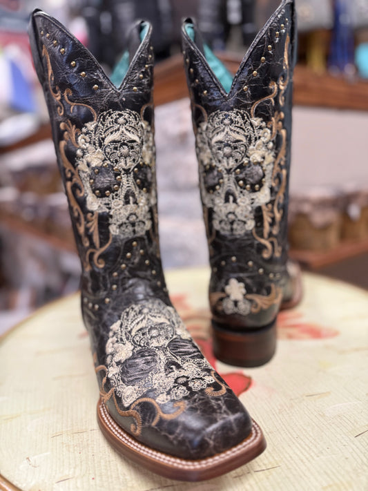 Pair of black cowboy boots with intricate designs on a wooden surface.