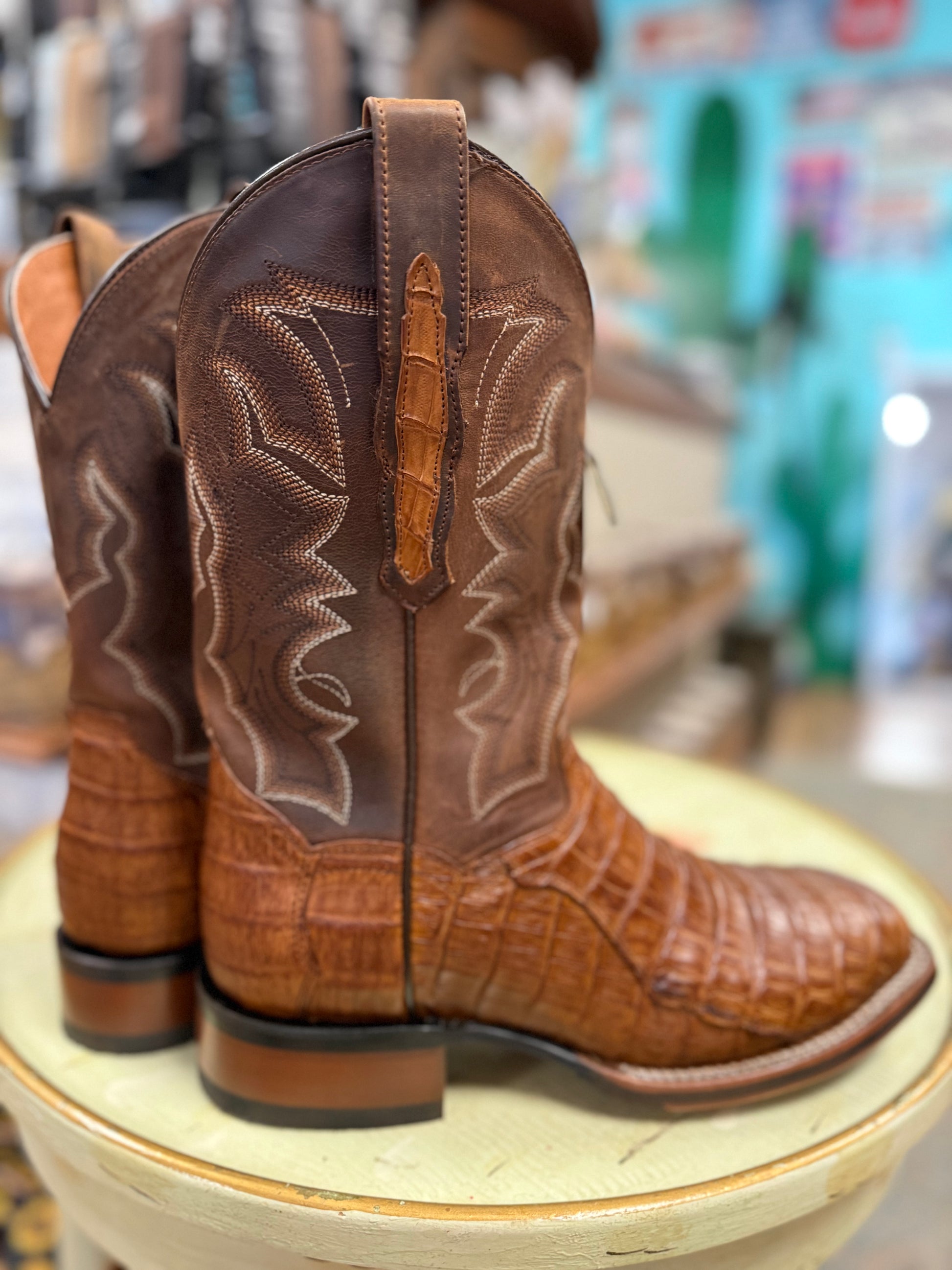 Brown cowboy boots with detailed stitching on a round surface, blurred store interior in the background