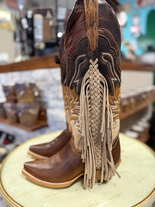 Brown cowboy boots with intricate designs and fringes on a round surface in a store setting.