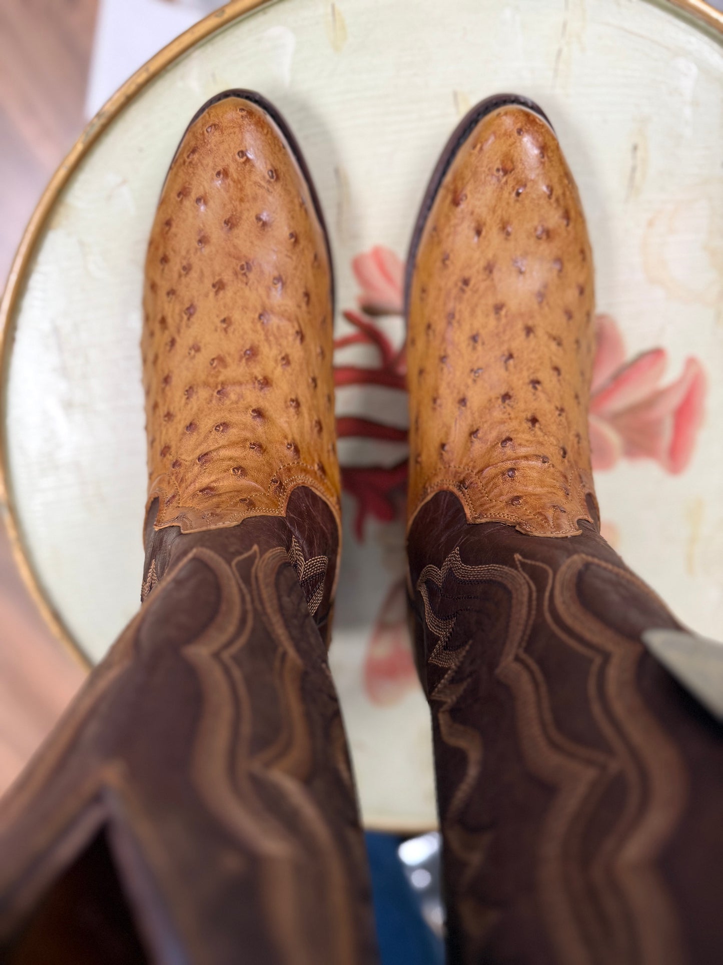 Brown and tan cowboy boot on a round white surface with a blurred store background