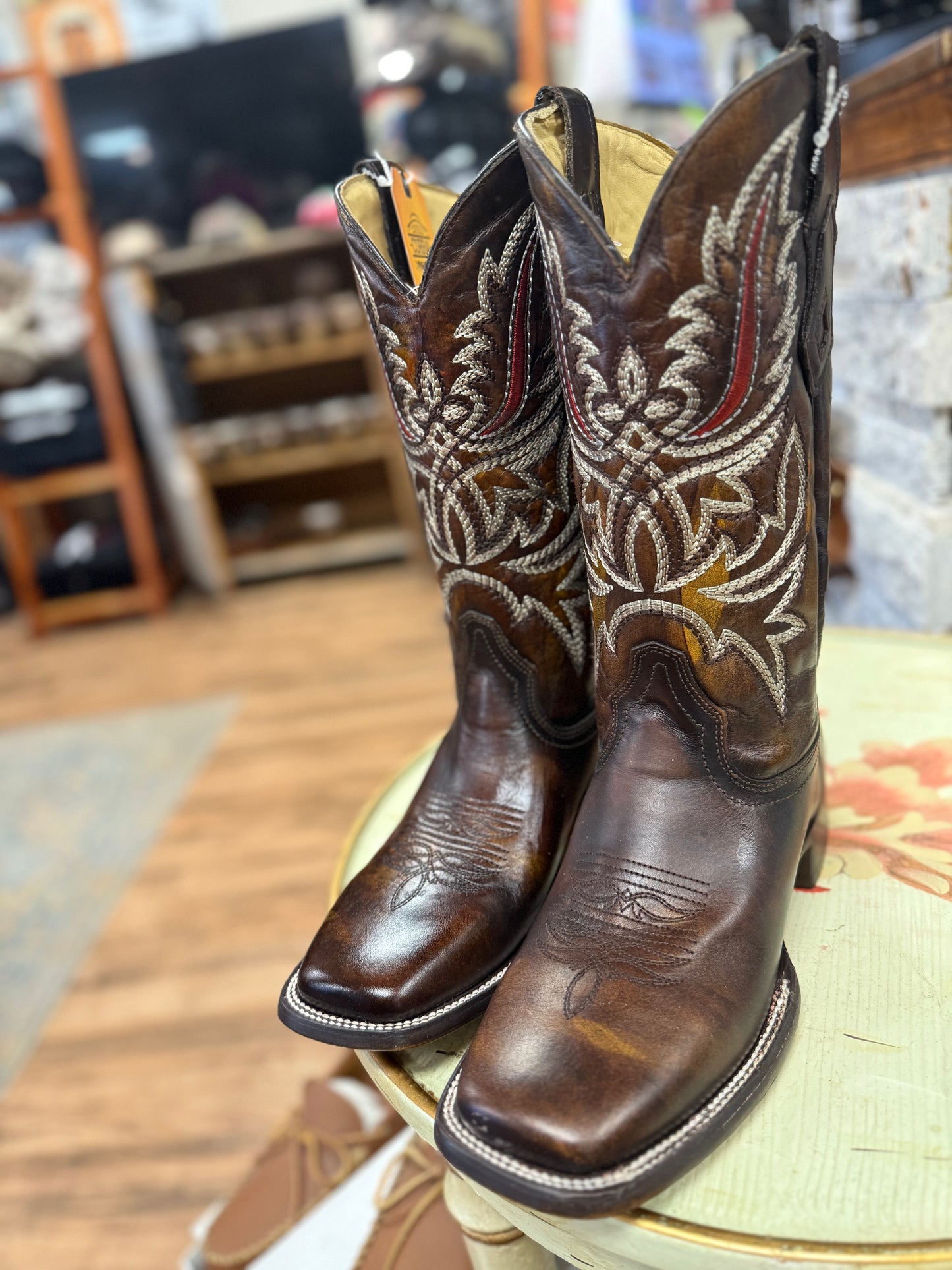 Pair of brown cowboy boots with intricate white embroidery on a stool in an indoor setting.