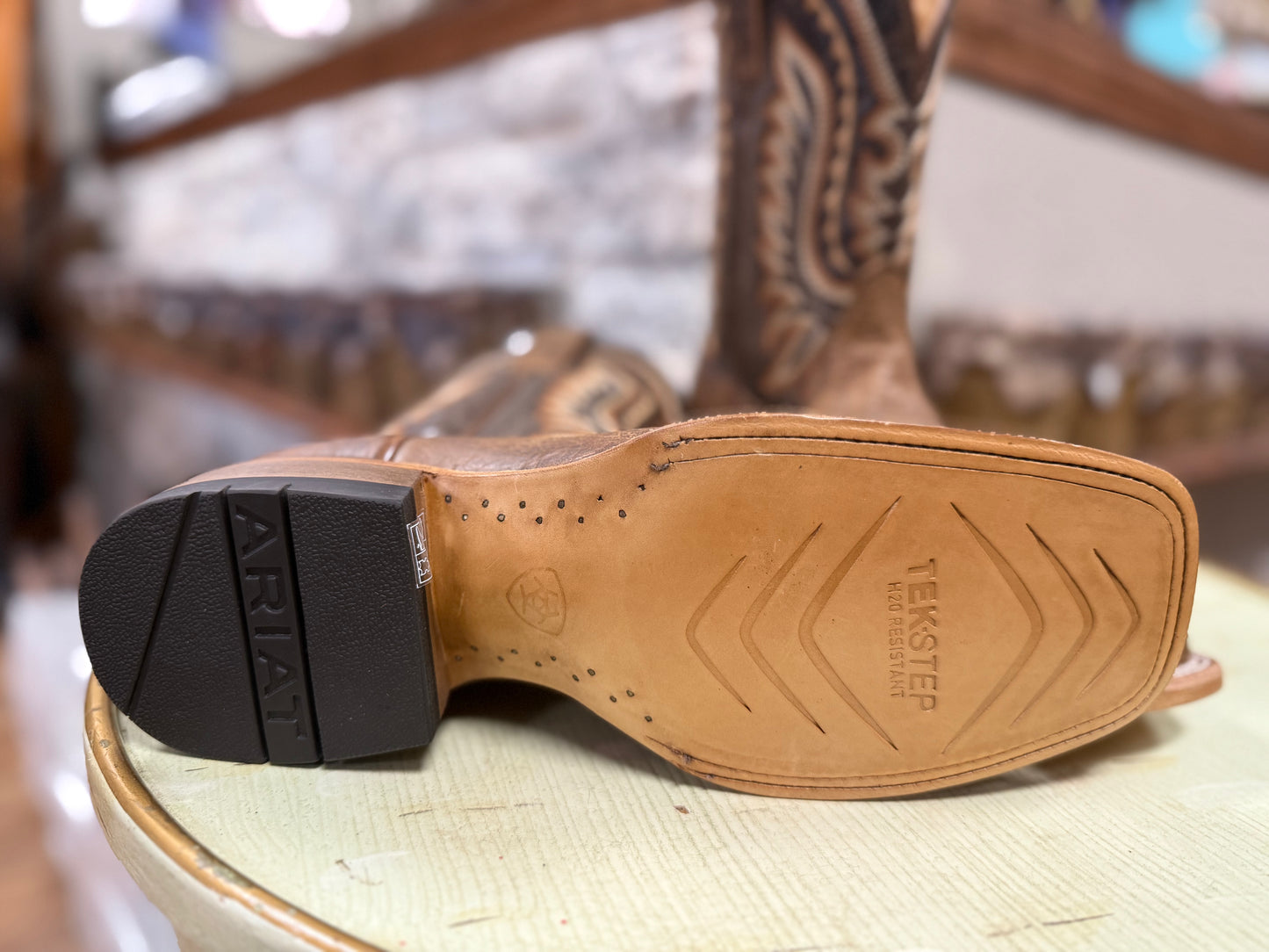 Close-up of a cowboy boot sole with Ariat branding on a blurred background