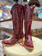 Red cowboy boots with intricate designs on a round surface in a store setting.