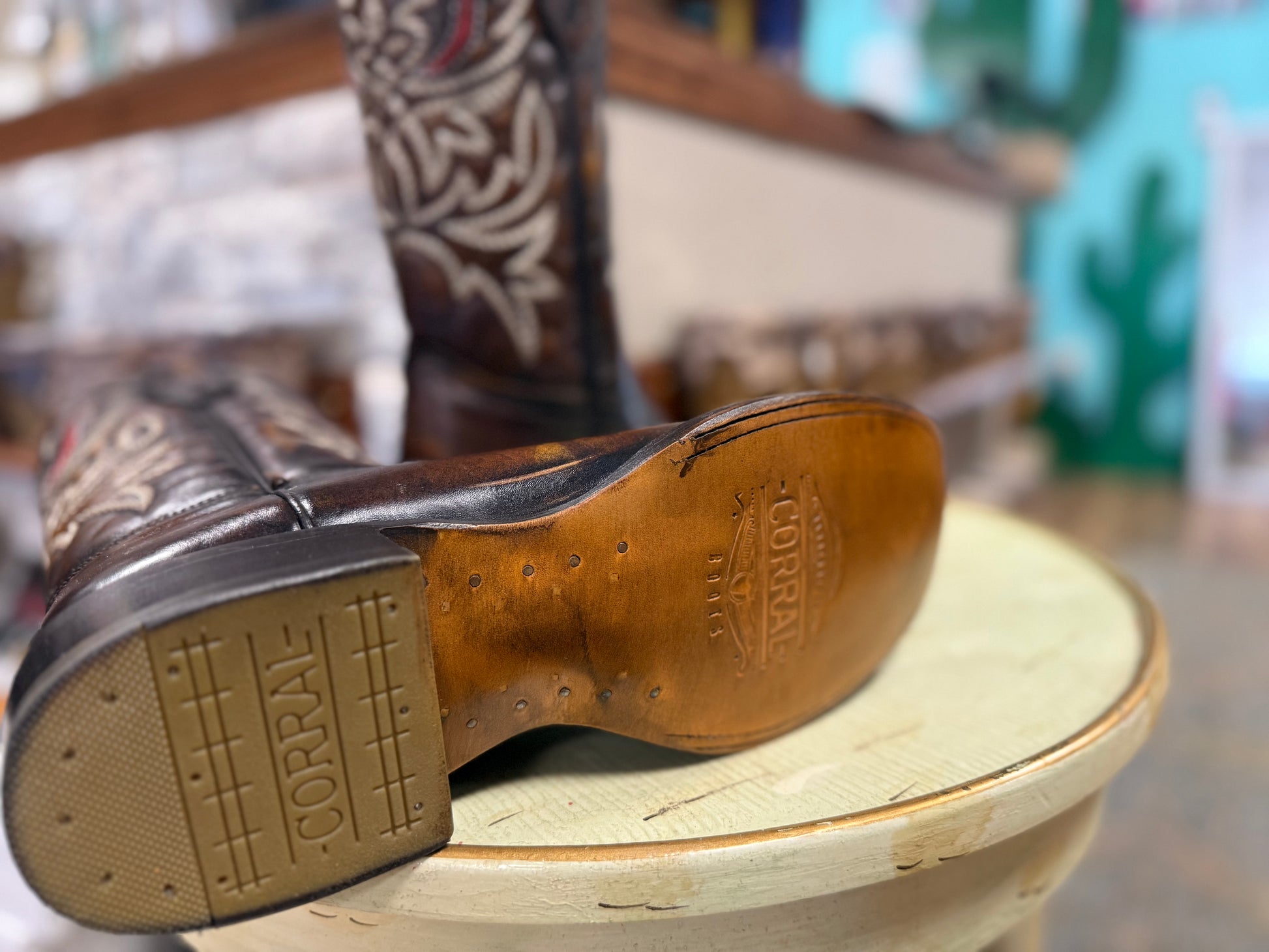 Close-up of a brown leather boot sole with 'Corral' branding on a wooden stool.