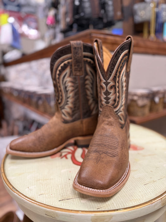 Brown cowboy boots with intricate designs on a round surface in a store setting.