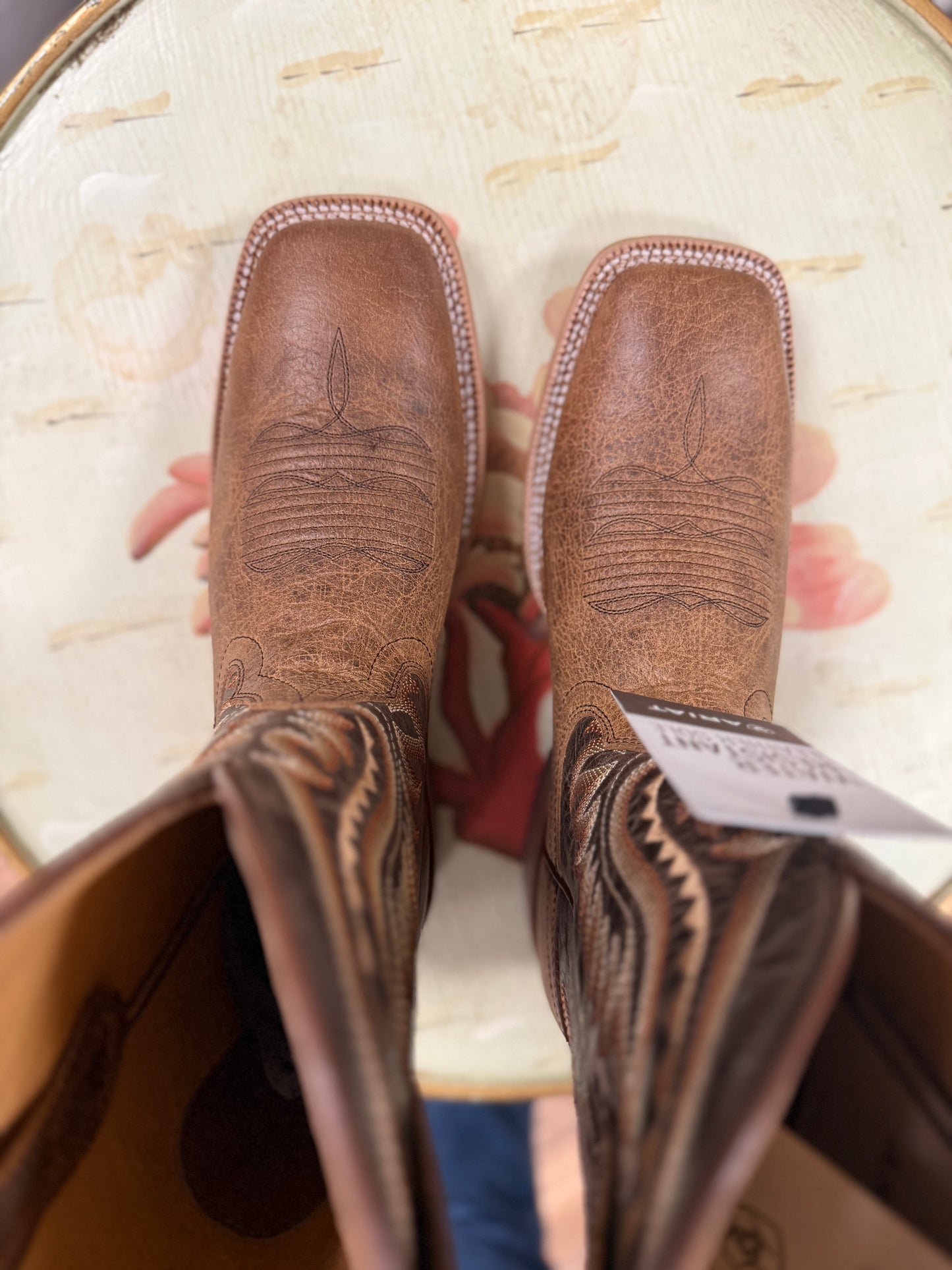 Brown leather boots with intricate designs held in a box.
