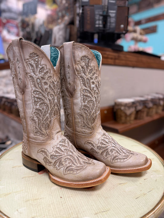Pair of beige cowboy boots with intricate designs on a wooden stool.