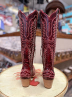Pair of red cowboy boots with intricate designs on a round wooden surface.