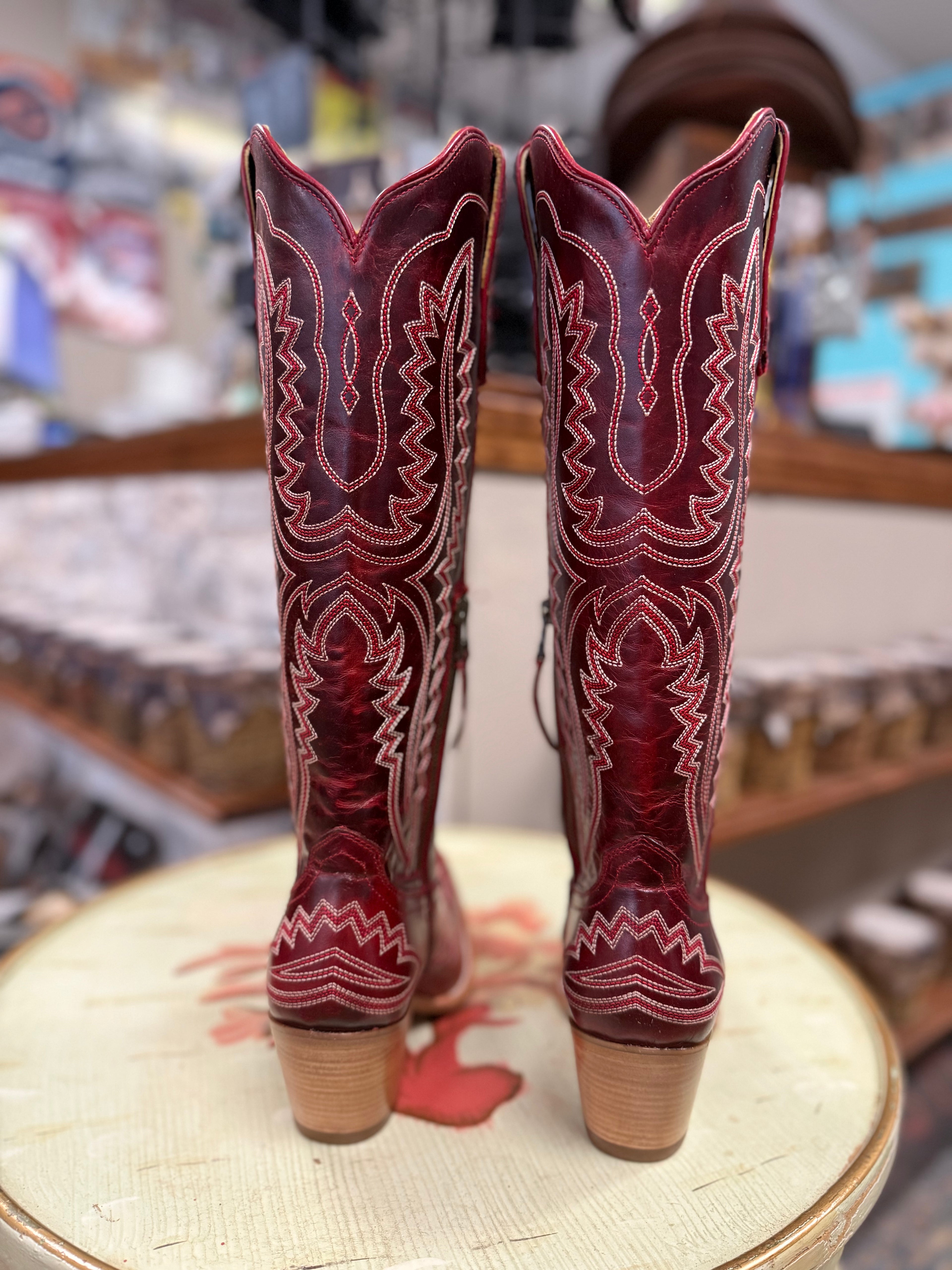 Pair of red cowboy boots with intricate designs on a round wooden surface.