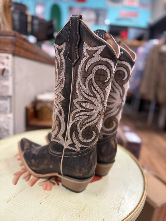 Pair of brown cowboy boots with intricate white embroidery on a round surface.
