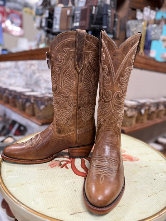 Pair of brown cowboy boots with intricate designs on a stool in a store setting.