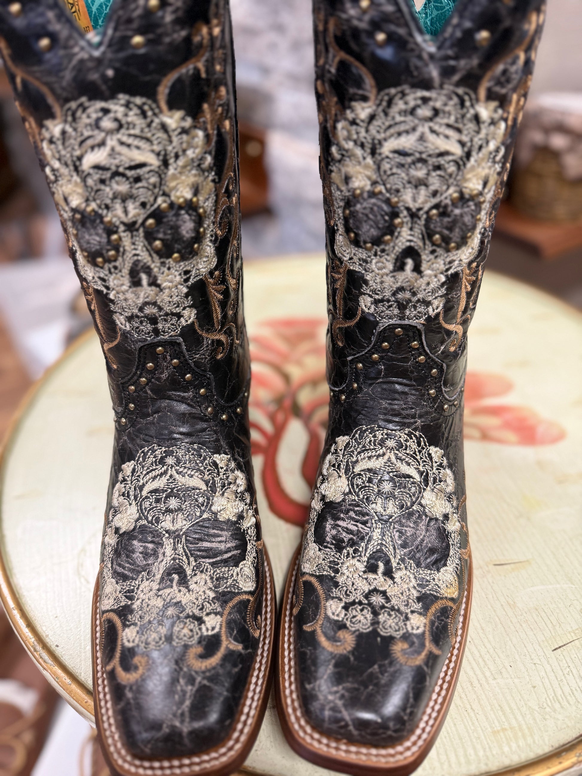 Decorative cowboy boots with skull designs on a floral cushion.
