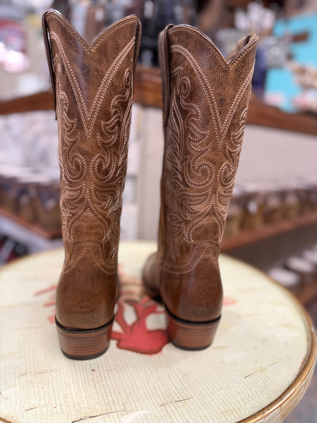 Pair of brown cowboy boots with intricate designs on a chair.