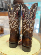 Pair of brown cowboy boots with intricate white embroidery on a round surface.