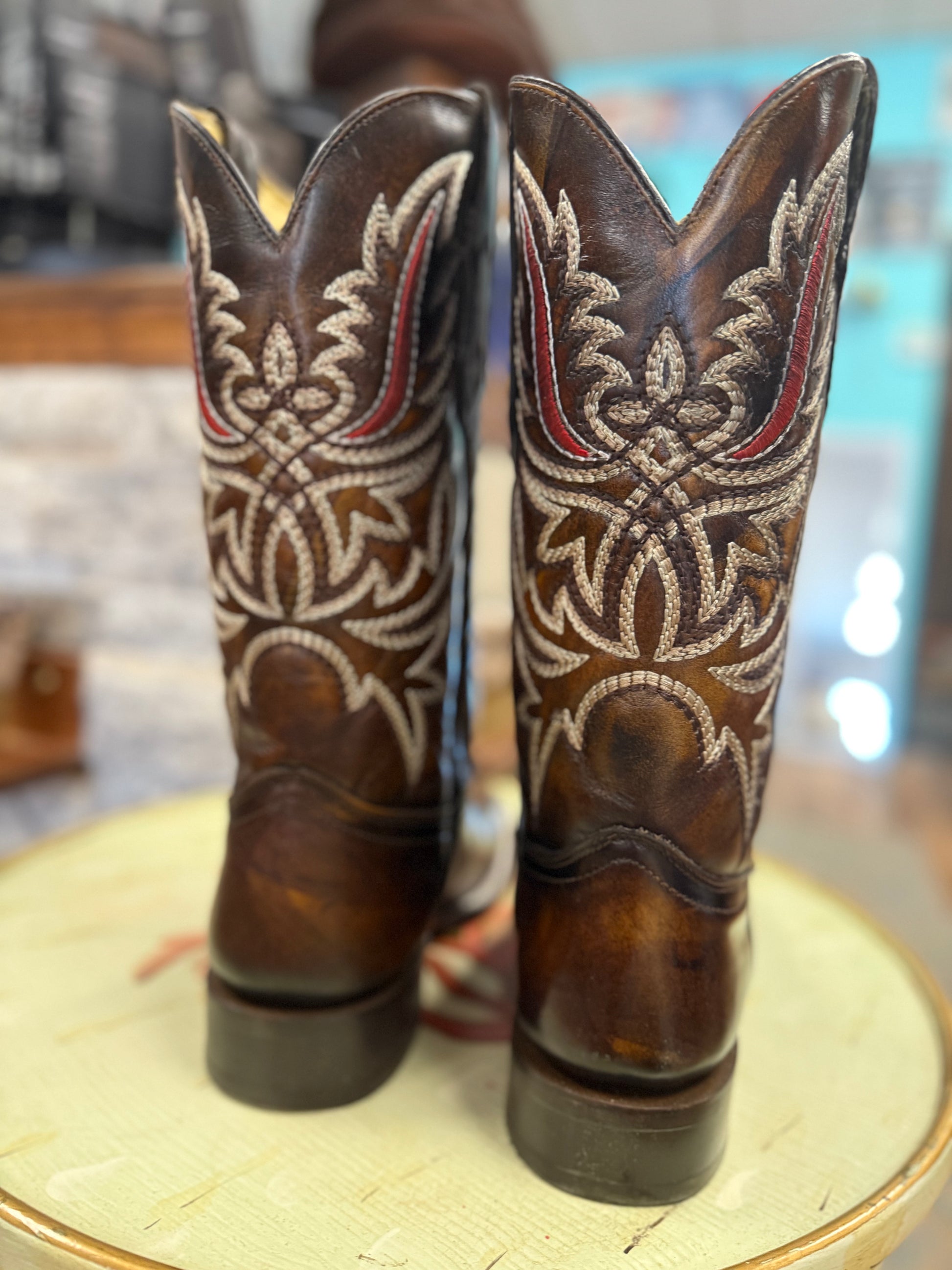 Pair of brown cowboy boots with intricate white embroidery on a round surface.