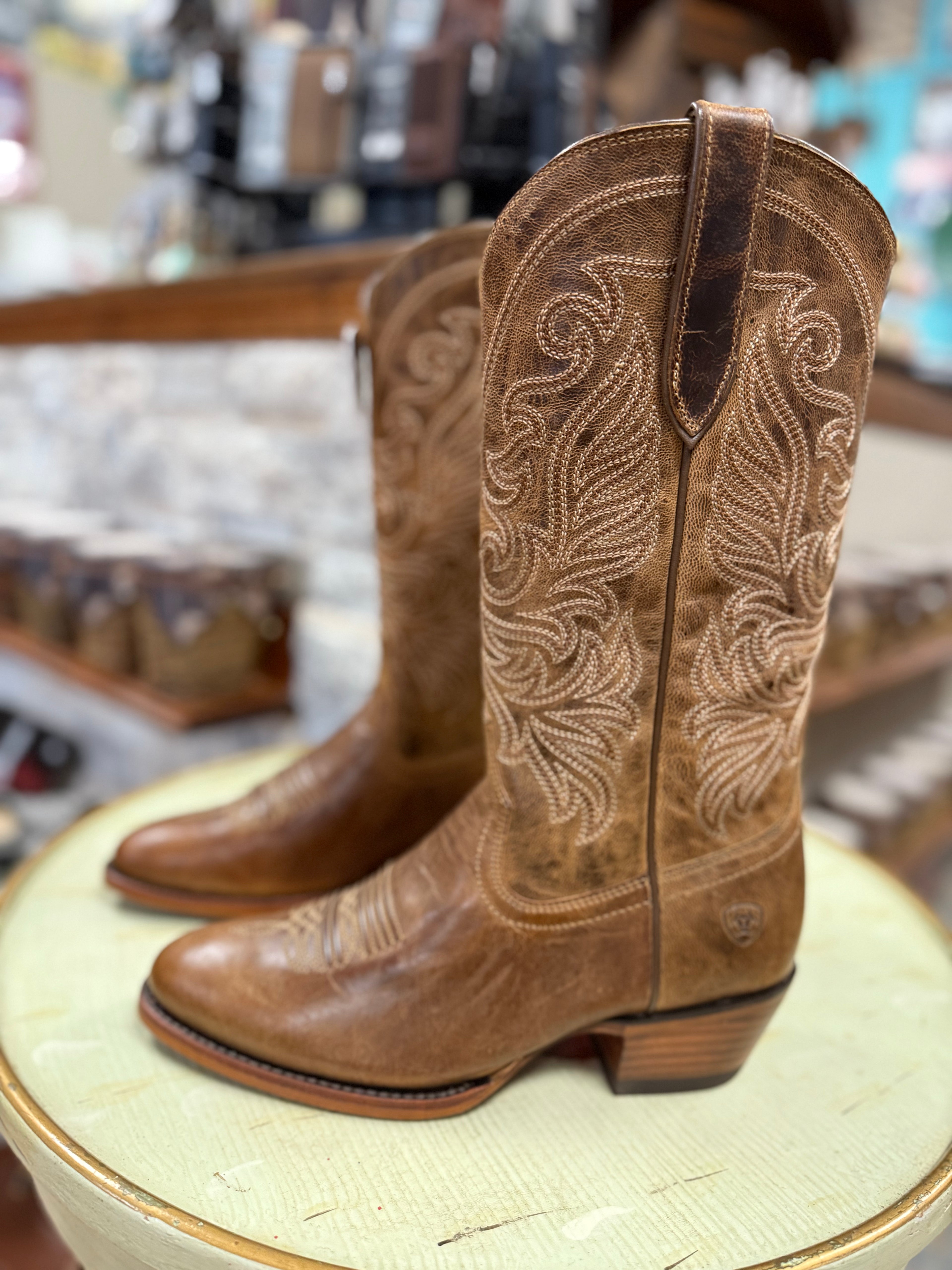 Pair of brown cowboy boots with intricate designs on a round surface.