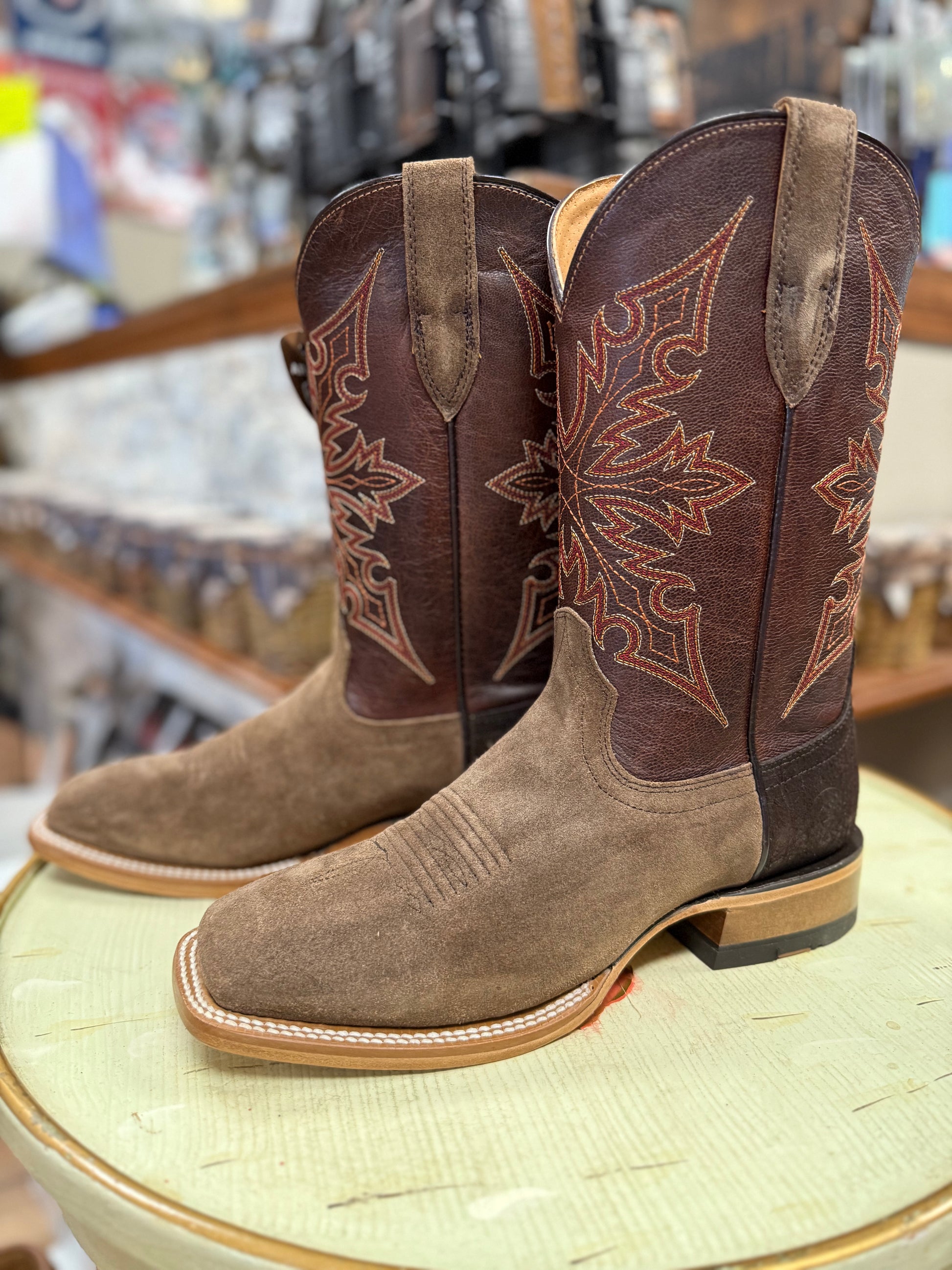 Pair of brown and tan cowboy boots with intricate designs on a round surface.