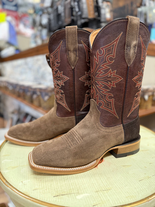 Pair of brown and tan cowboy boots with intricate designs on a round surface.