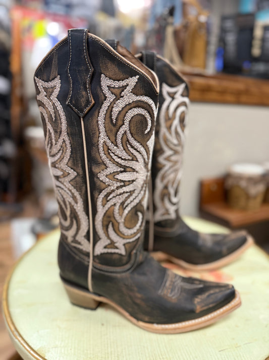 Pair of cowboy boots with intricate white embroidery on a green cushion