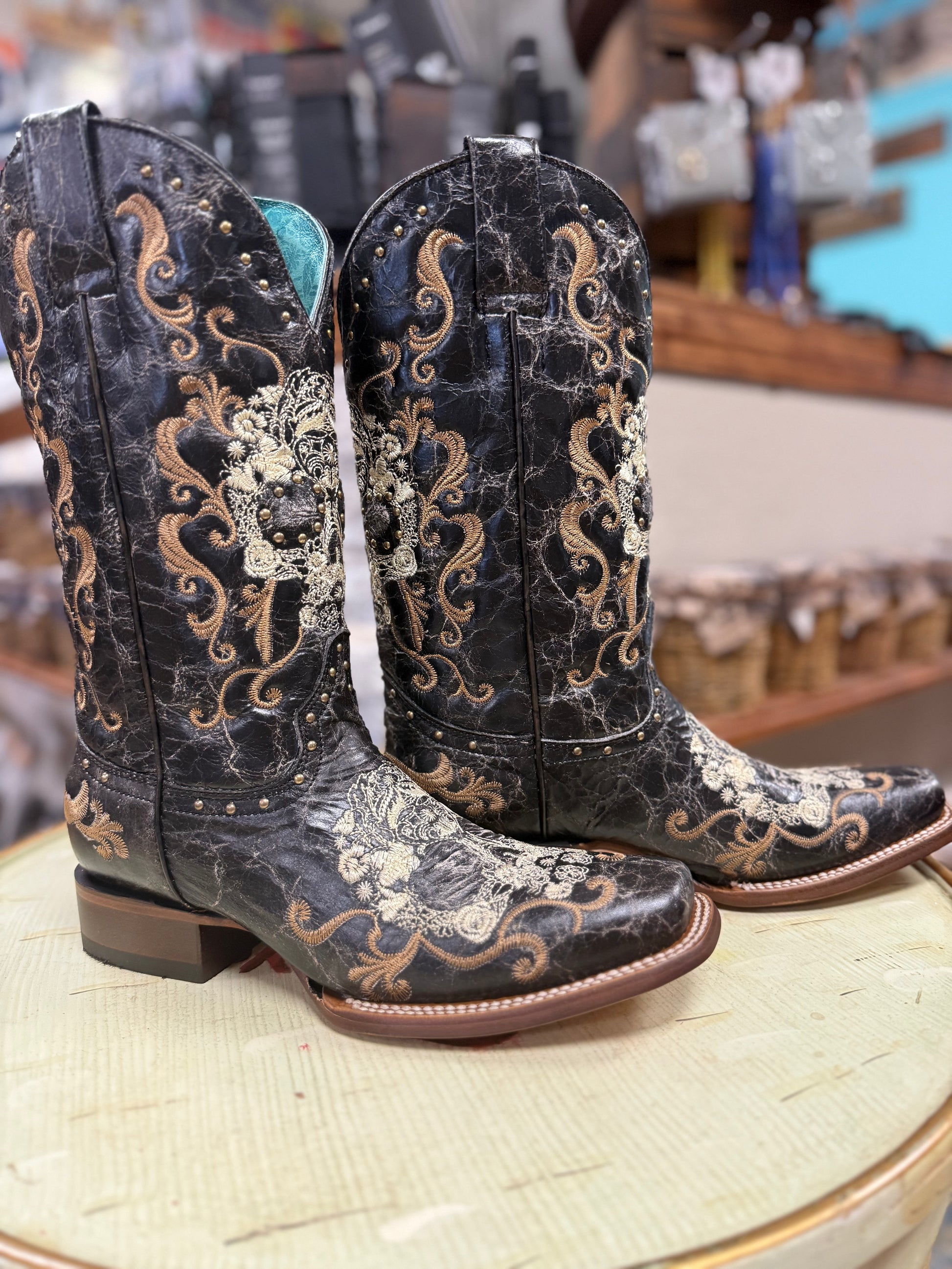 Pair of black cowboy boots with intricate gold embroidery on a wooden surface.