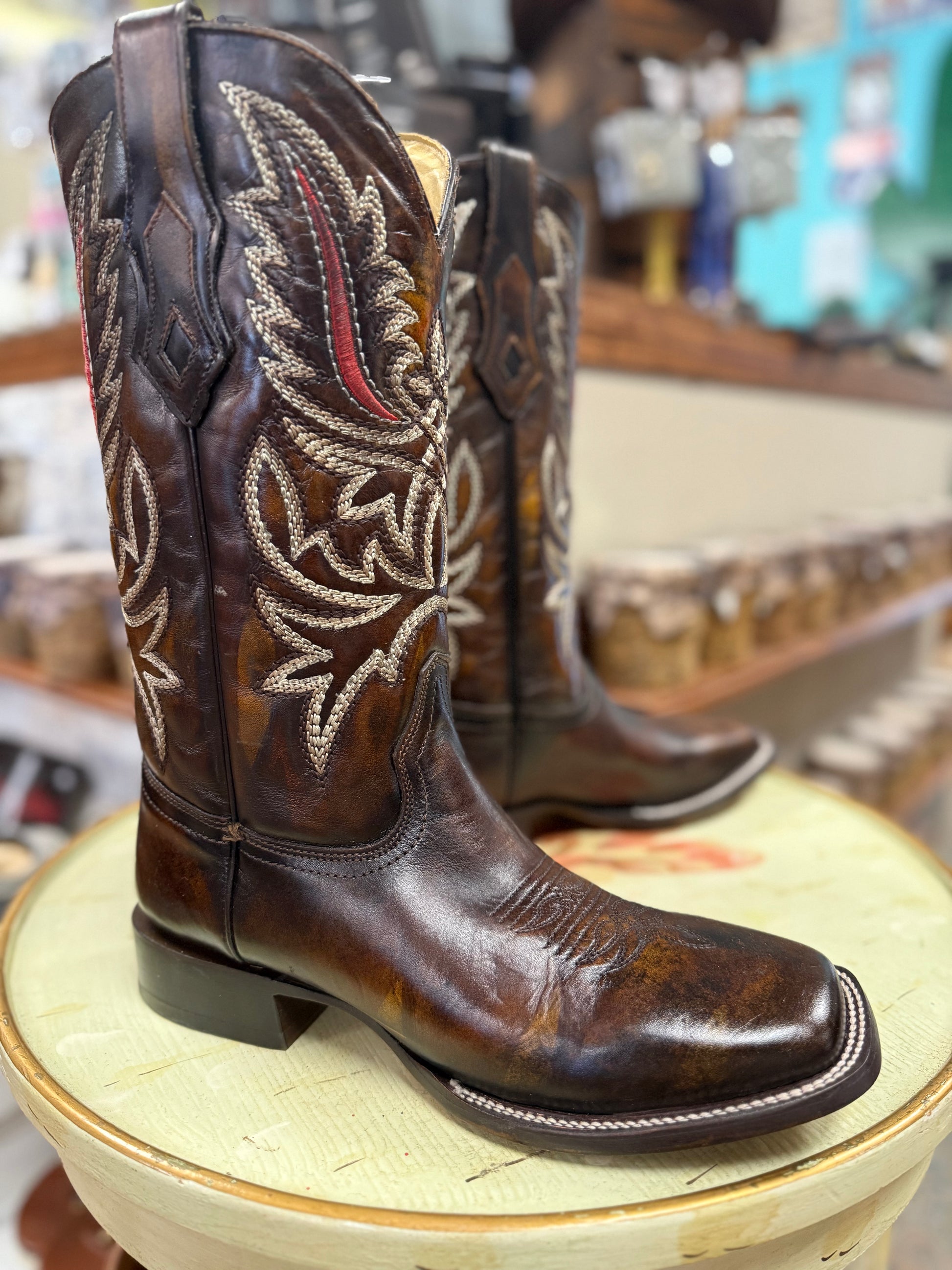 Brown cowboy boots with intricate white stitching on a green stool.
