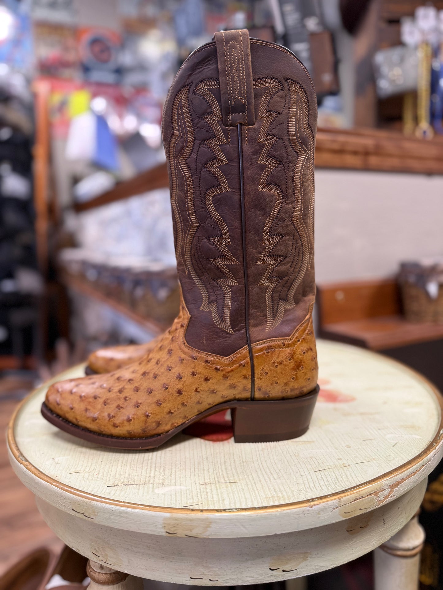 Brown and tan cowboy boot on a round white surface with a blurred store background